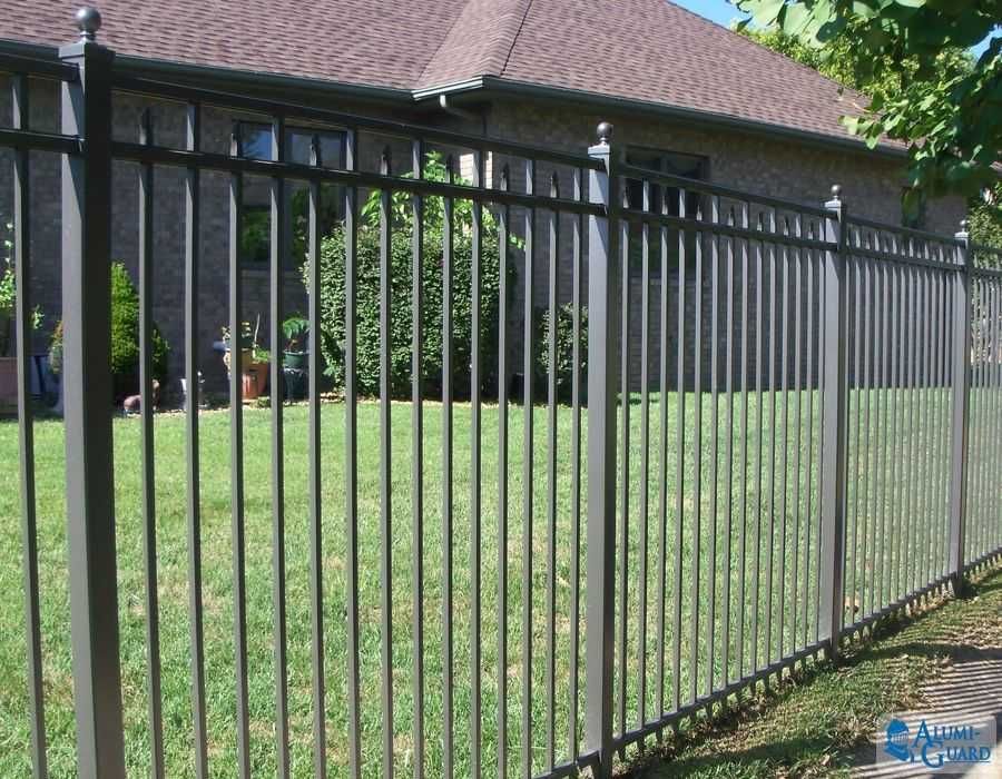 A metal fence surrounds a lush green yard in front of a house