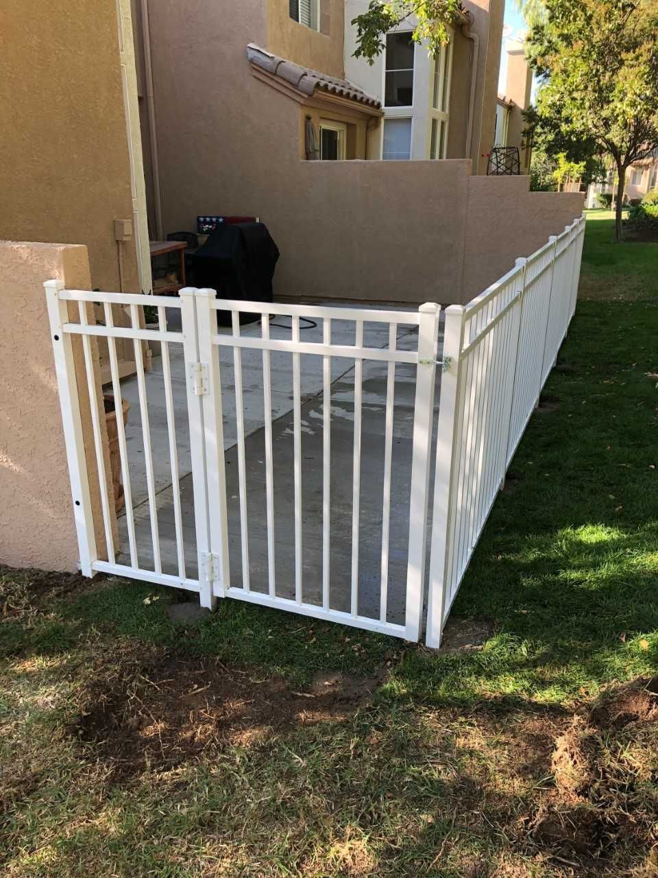 A white fence is surrounding a patio with a grill.