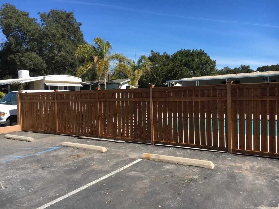 A wooden fence is surrounding a parking lot next to a pool.