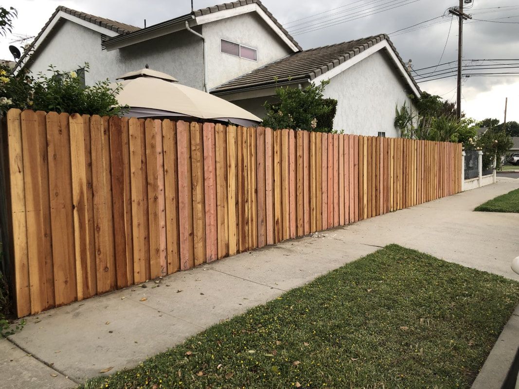 A wooden fence is along the sidewalk in front of a house.