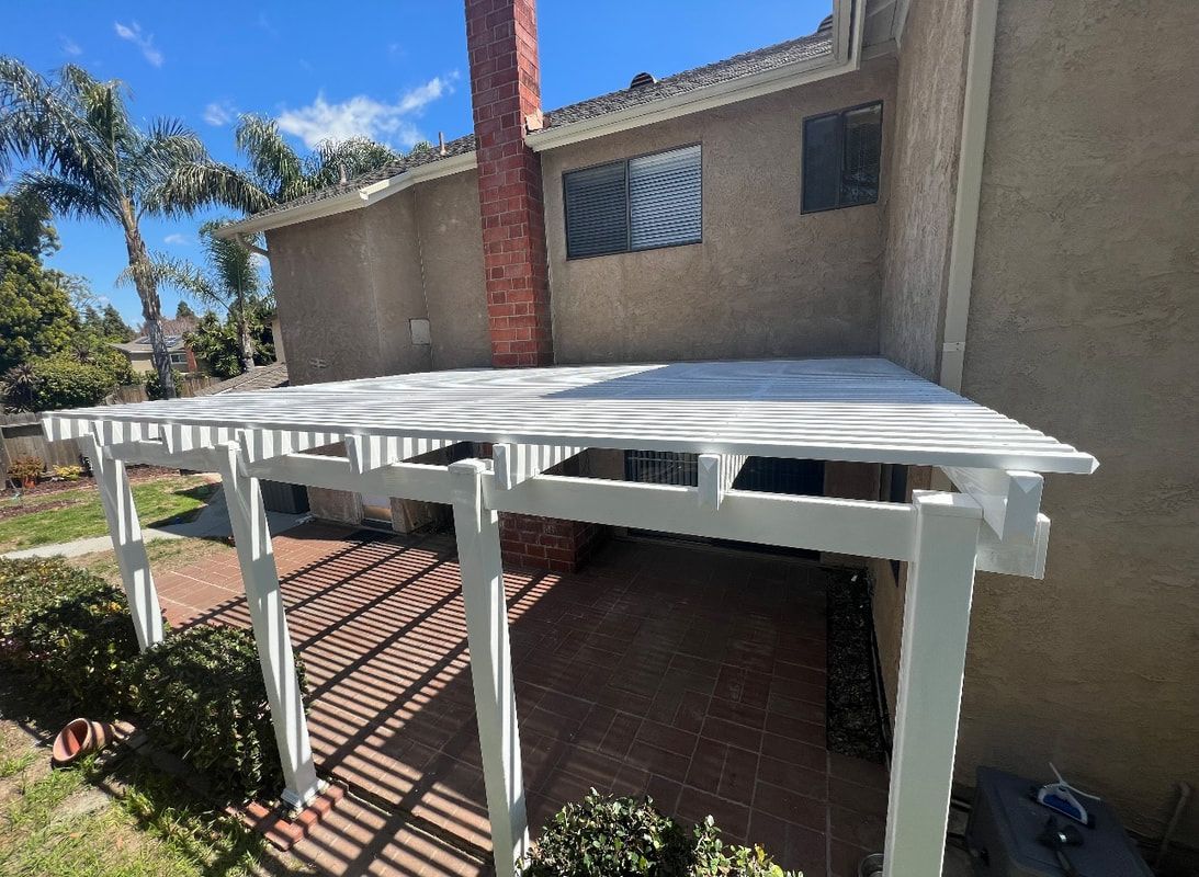 A white pergola is sitting in front of a house.