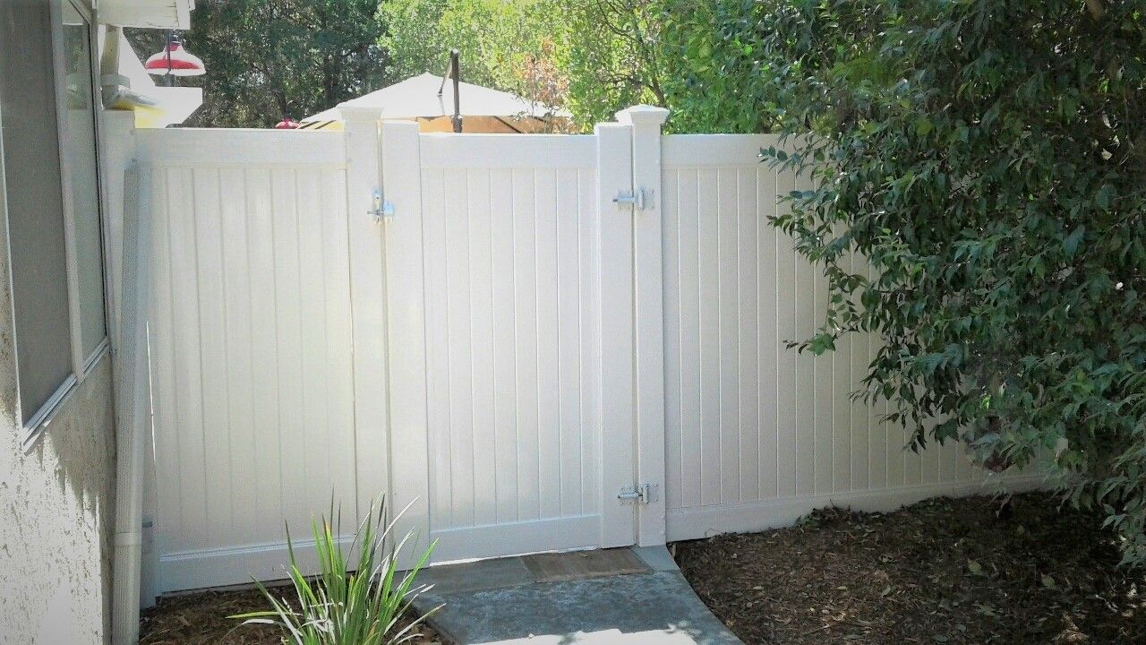 A white fence with a gate in the backyard of a house.