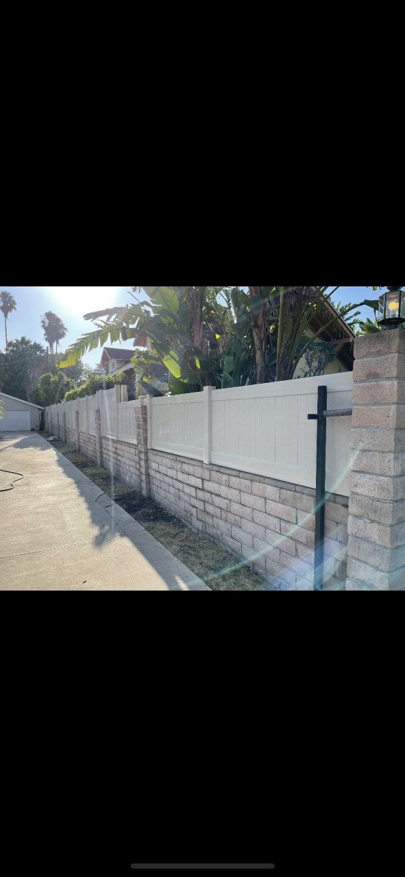 A white fence is sitting next to a brick wall.