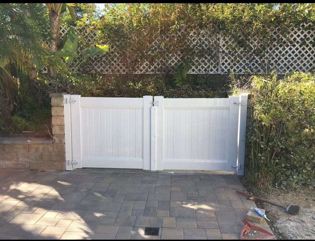 A white gate is sitting on a brick driveway next to a fence.