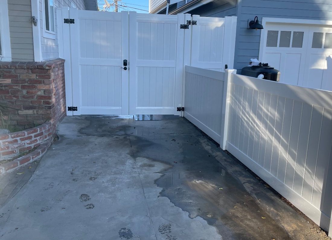 A white fence is sitting next to a brick wall and a garage door.