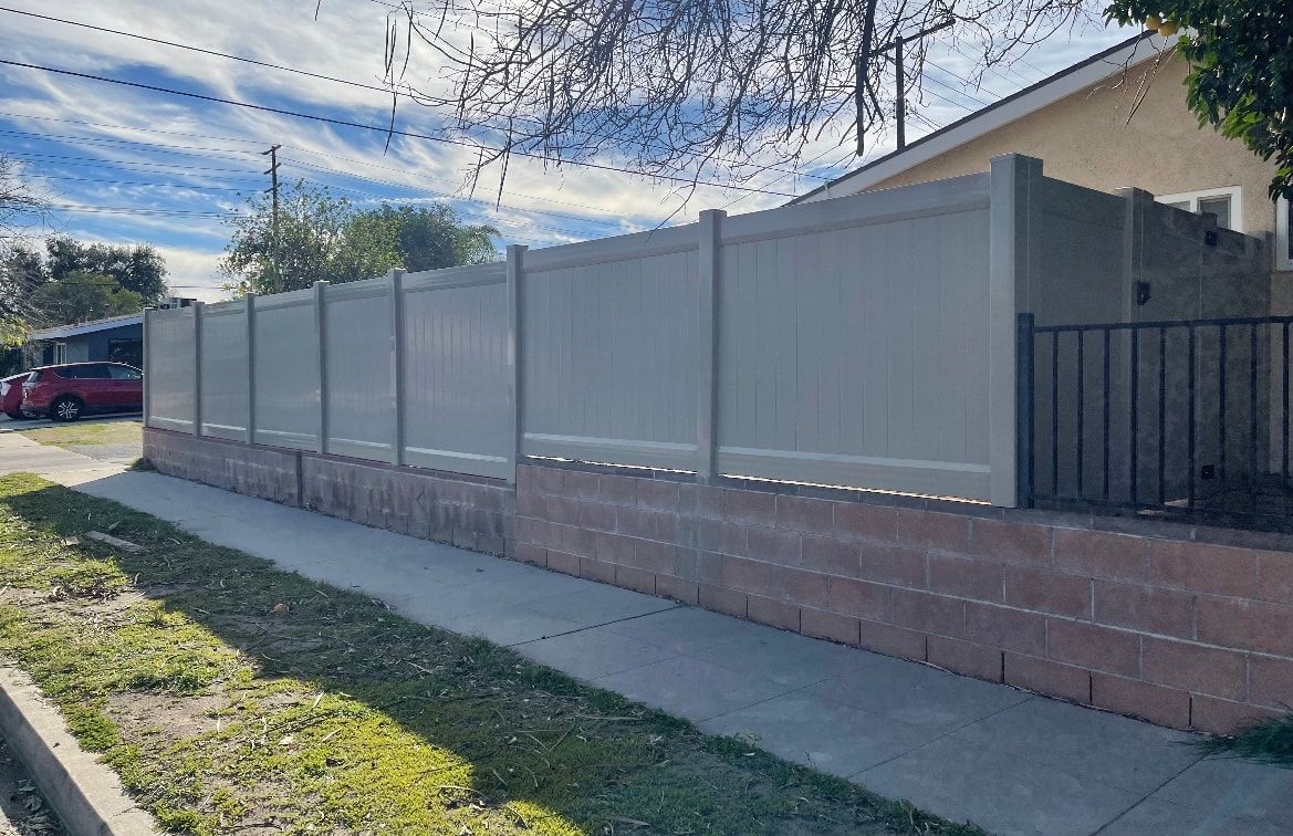 A white fence is surrounding a brick wall next to a sidewalk.
