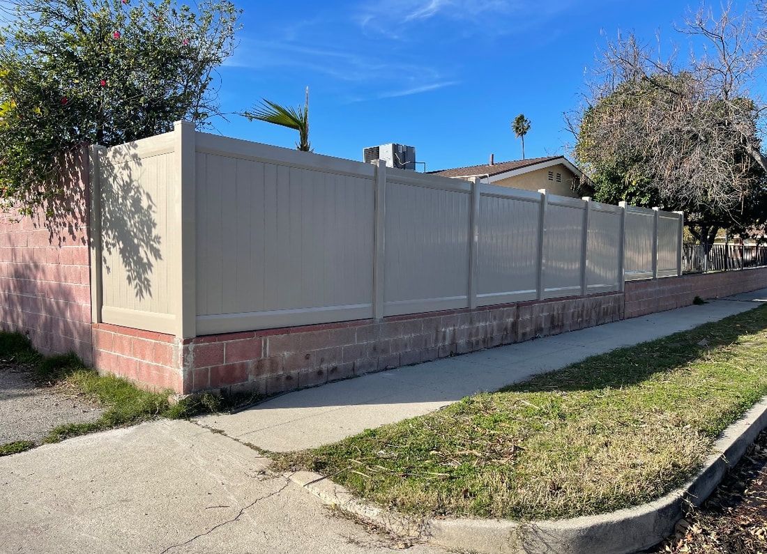 A white fence surrounds a brick wall next to a sidewalk.