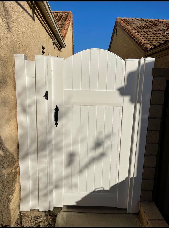 A white gate with a black handle is sitting next to a building.