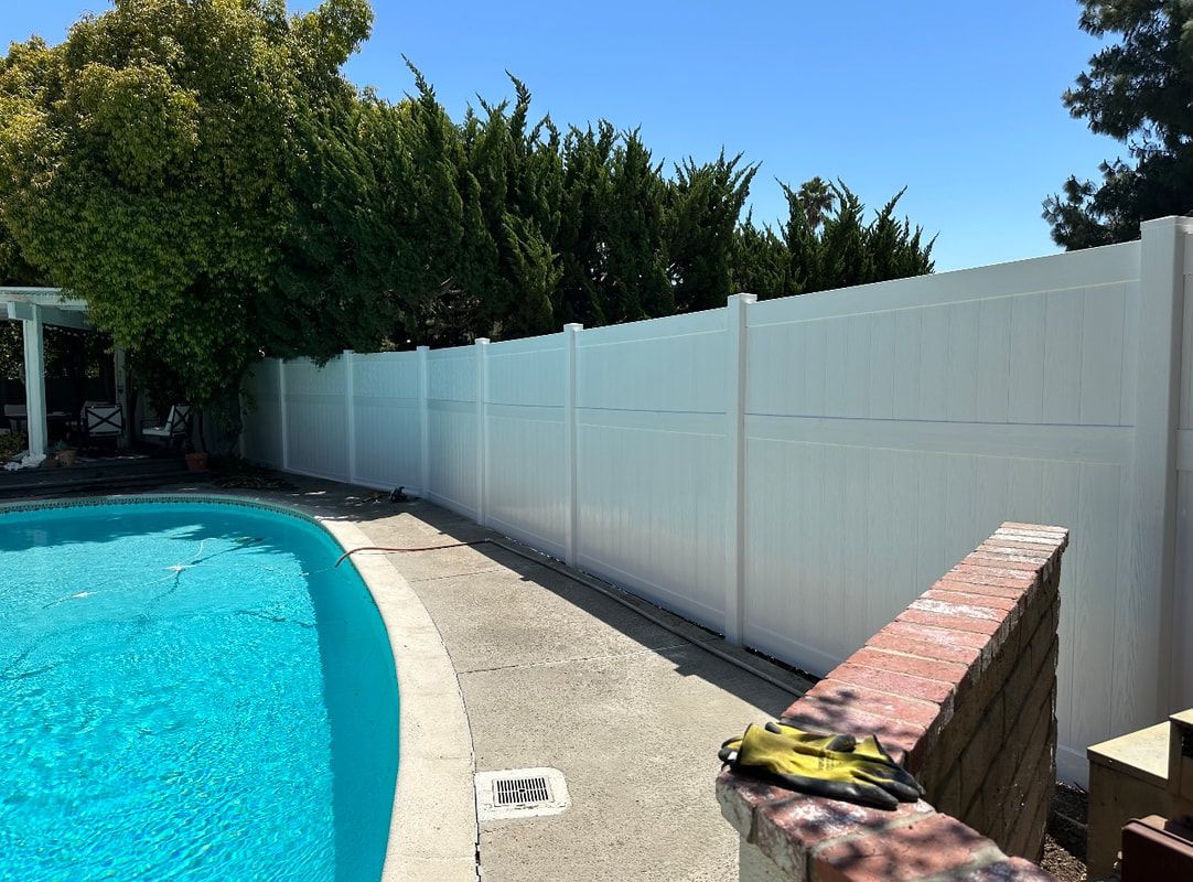 A white fence surrounds a large swimming pool.