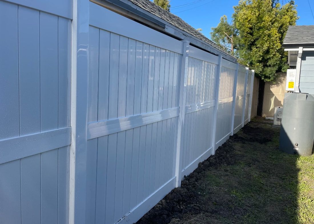 A white vinyl fence is sitting in the backyard of a house.