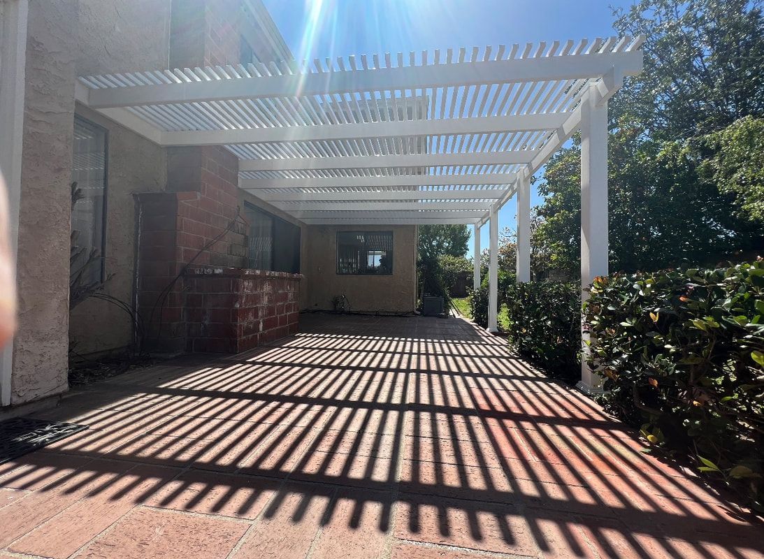 A person is standing under a white pergola in front of a house.