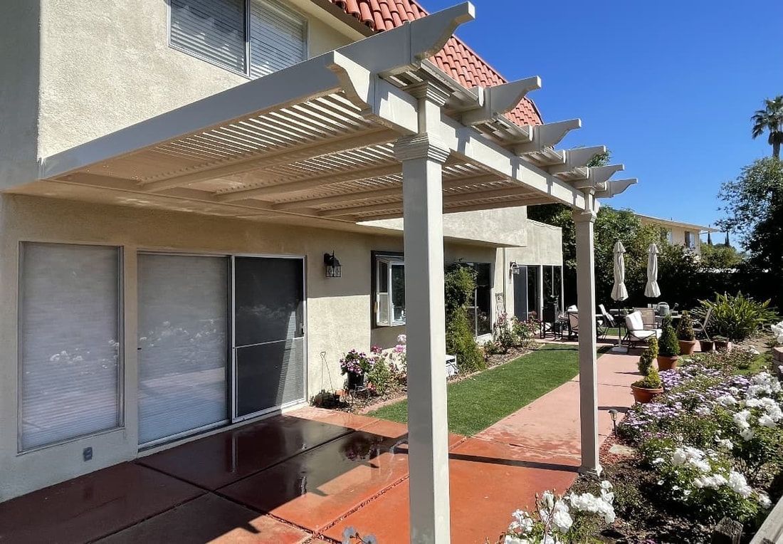 A white pergola is sitting on top of a patio in front of a house.