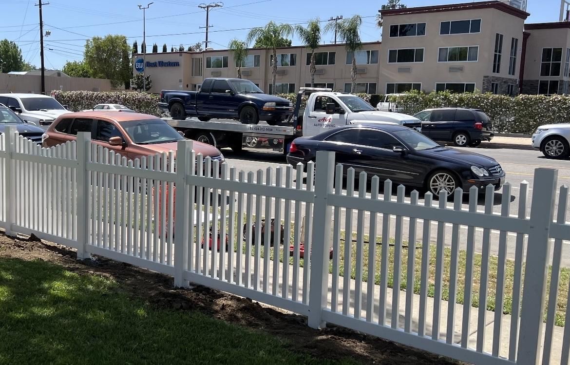 A white picket fence surrounds a parking lot with cars parked behind it.