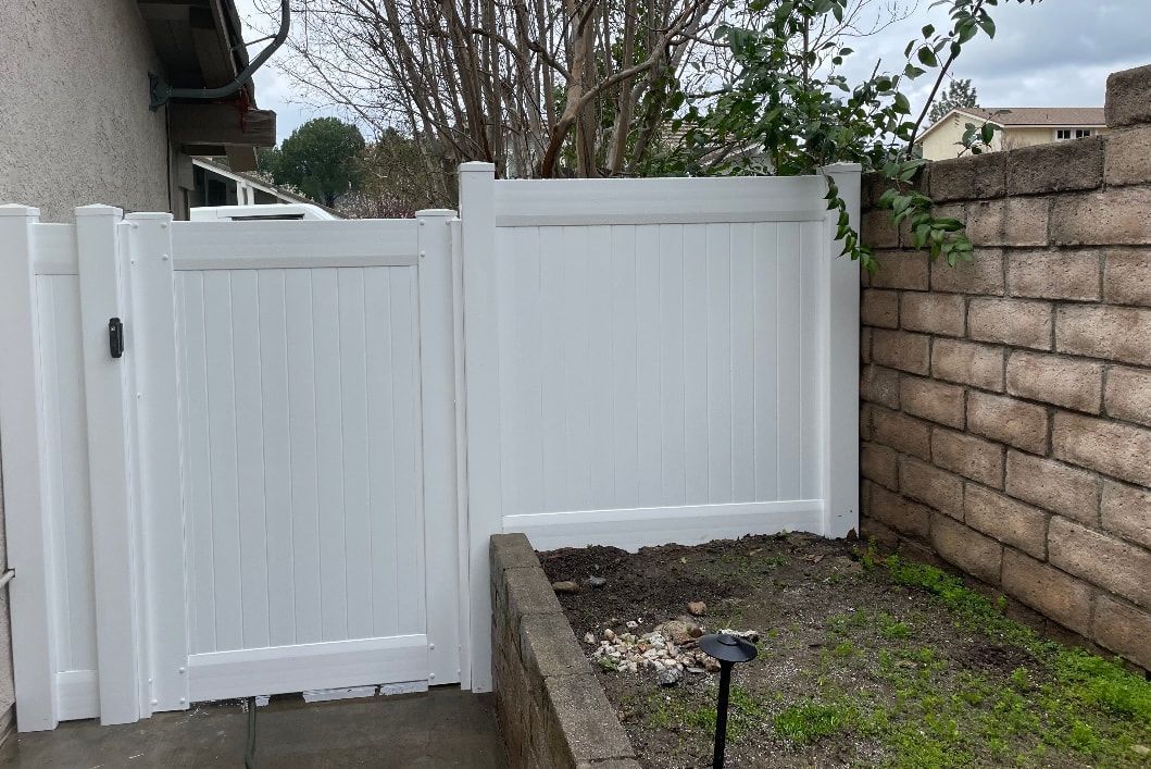 A white fence with a gate in the backyard of a house.