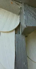 A close-up view of a transition area on a building exterior where gray wooden trim meets beige scalloped siding.