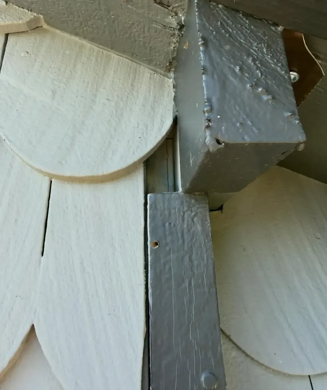 A close-up view of a transition area on a building exterior where gray wooden trim meets beige scalloped siding.