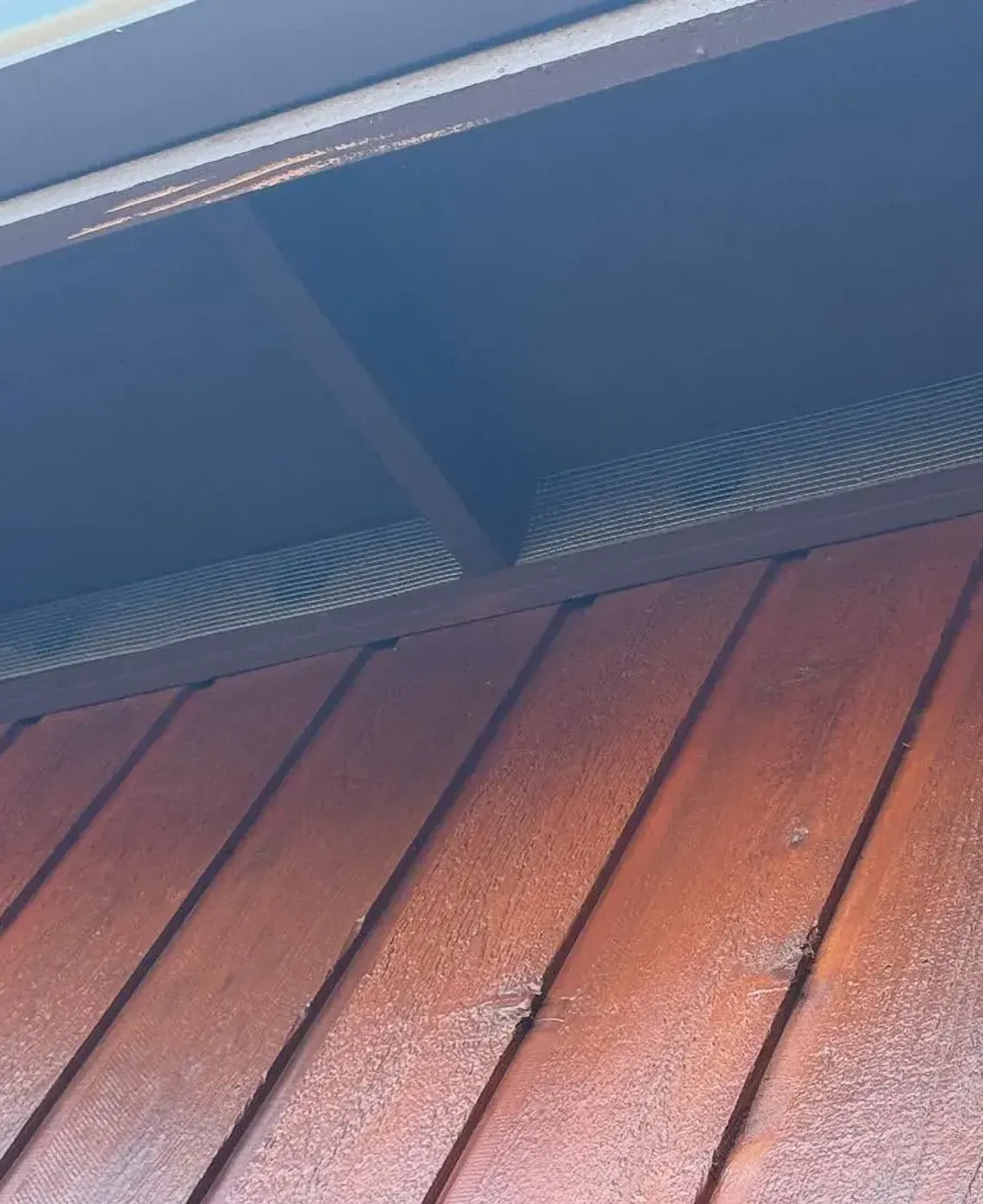 Low-angle view of a brown wooden house exterior, showing vertical siding and the dark, recessed eaves of the roof.