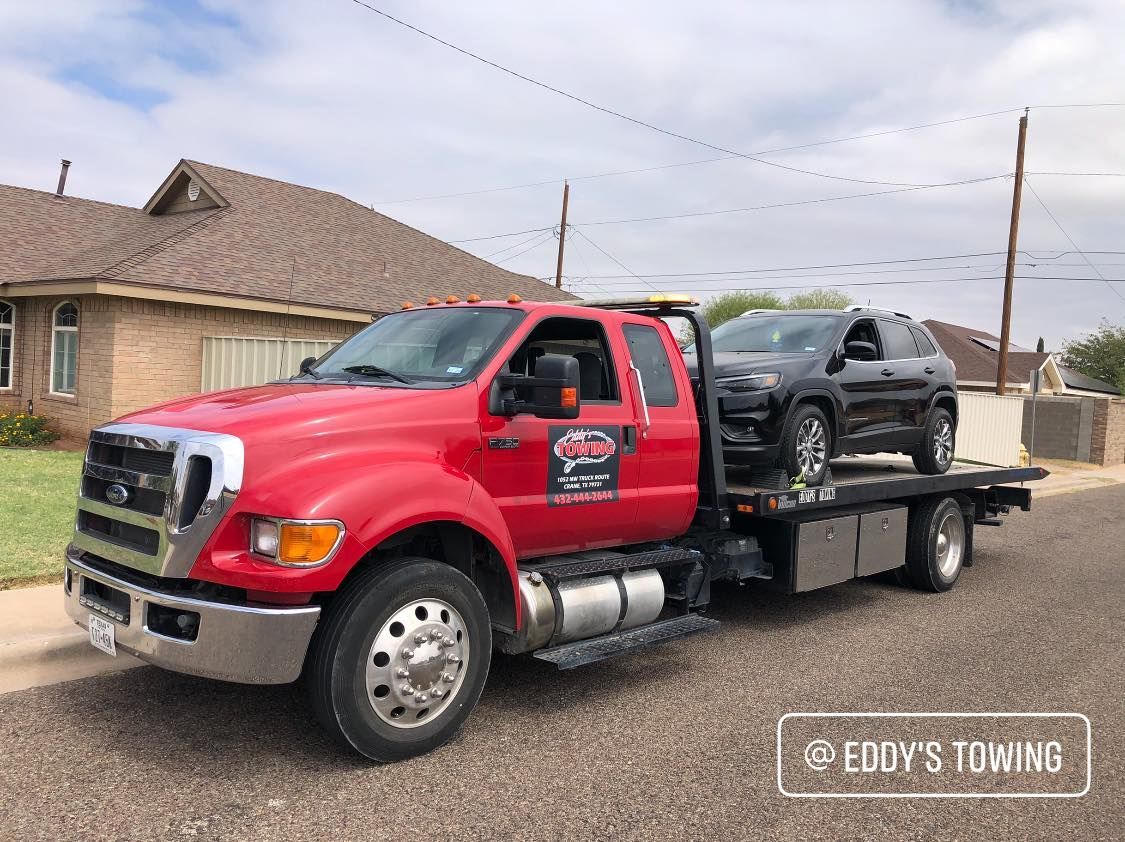 Red tow truck with a black SUV on its flatbed, parked in front of a house.