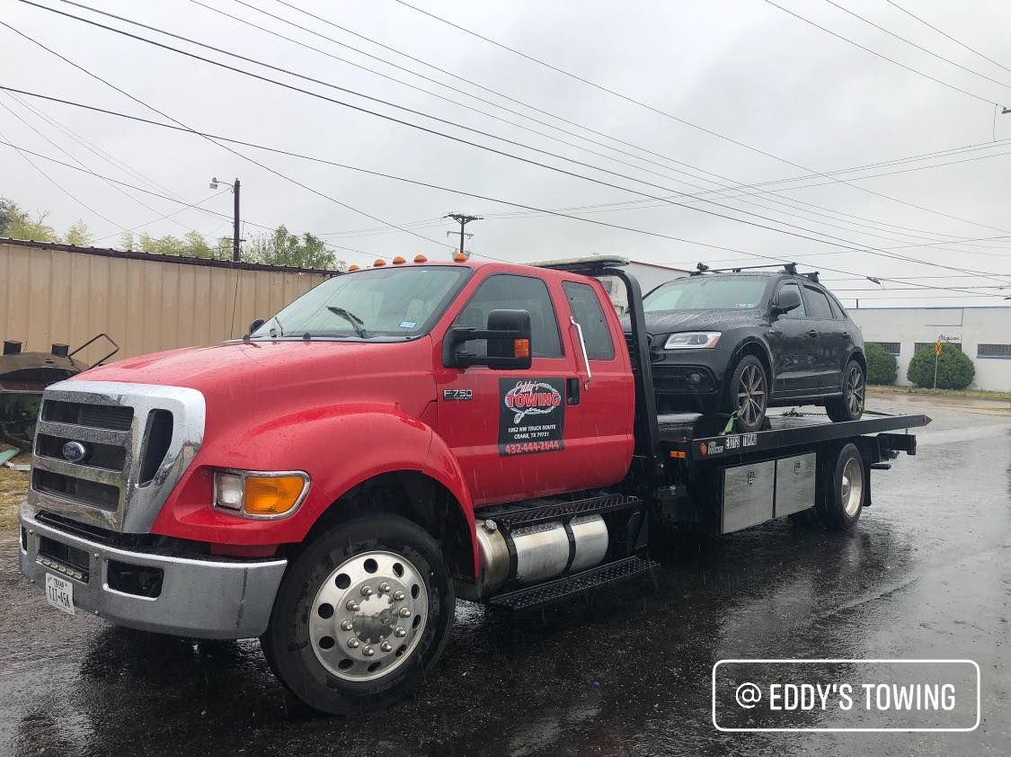 Red tow truck carrying a gray car on a wet day.