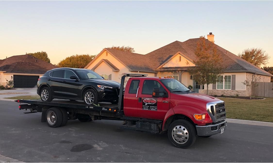 A red tow truck carrying a black SUV on a residential street.