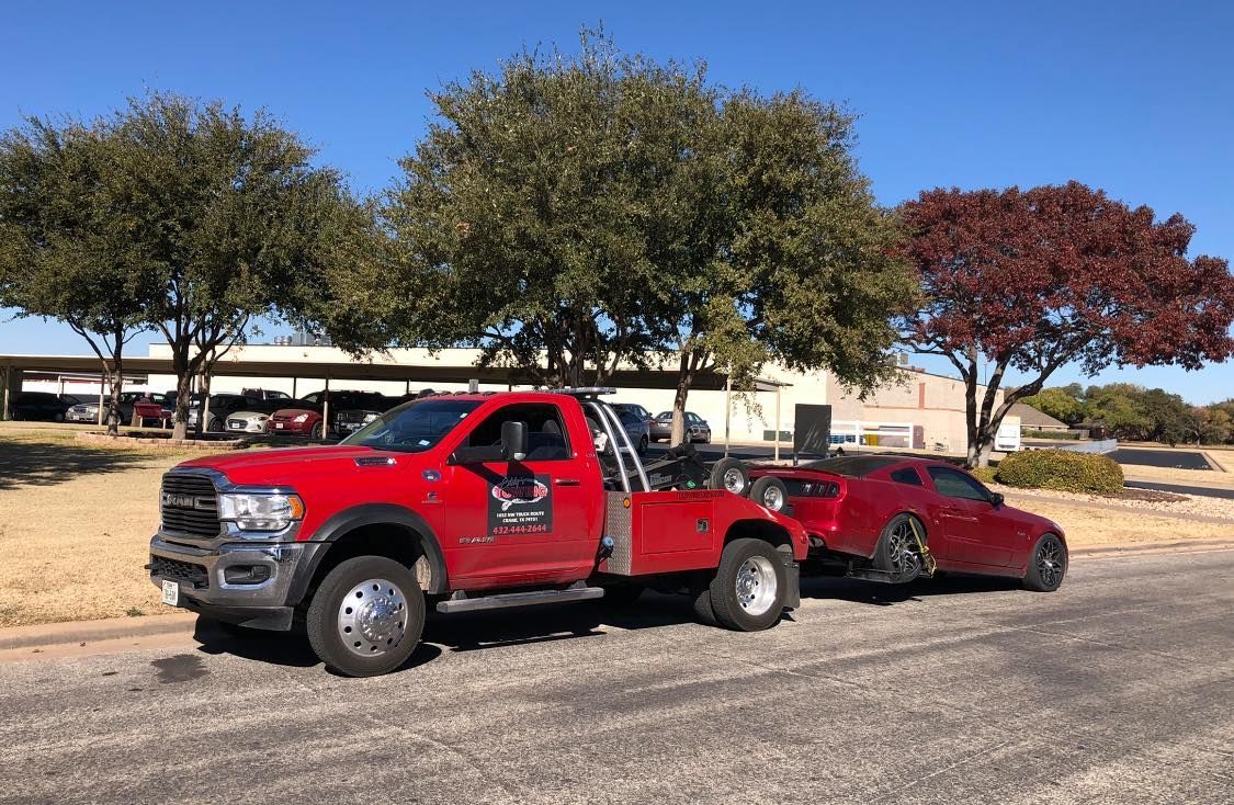 Red tow truck towing a red car on a paved road under sunny sky.