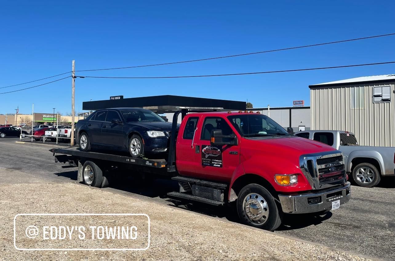 Red tow truck carrying a black car on a sunny day at a tow yard.