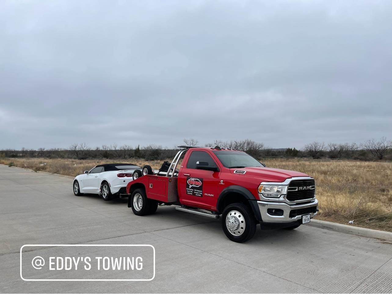 Red tow truck towing a white car on a road under a cloudy sky.