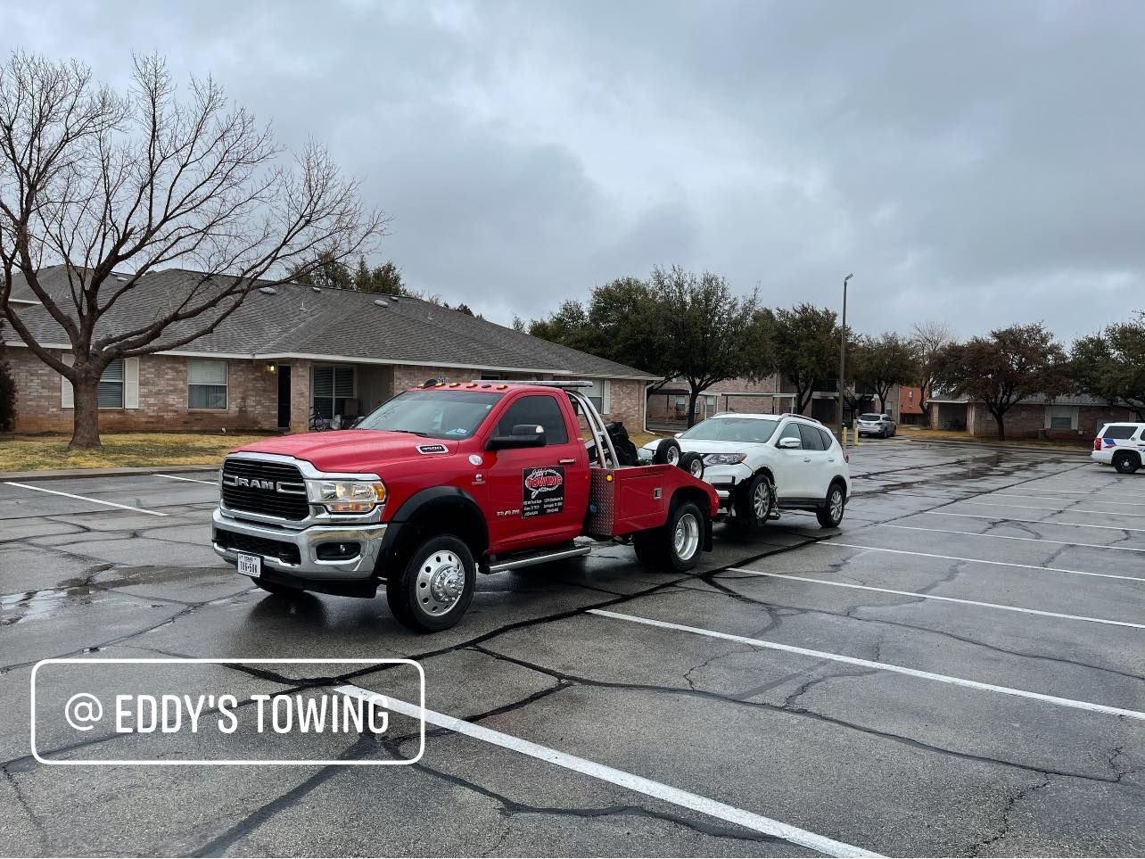 Red tow truck towing a white SUV in a parking lot on a cloudy day.