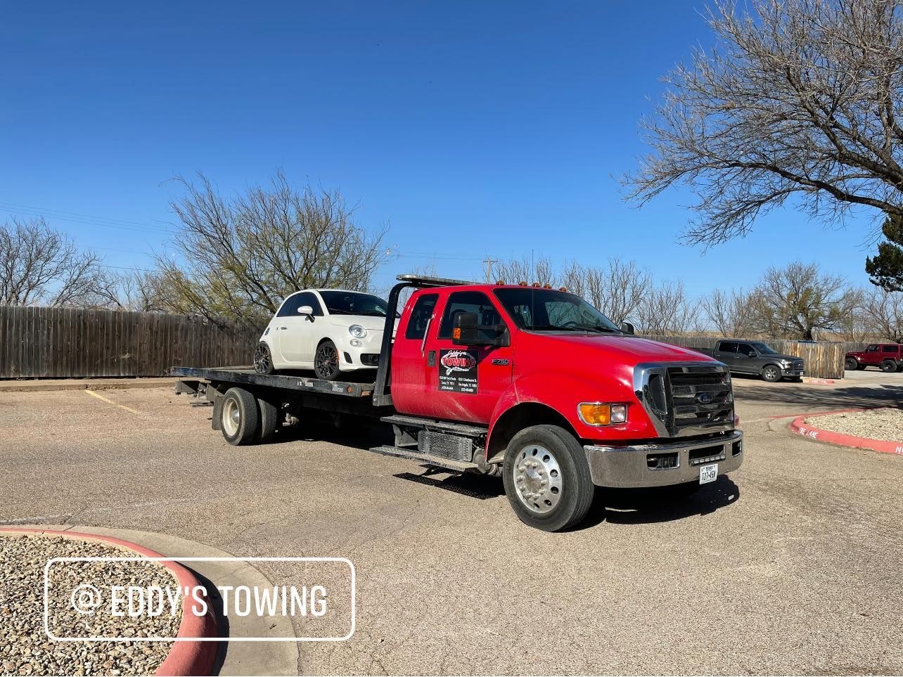 Red tow truck with a white car on its flatbed, under a blue sky.