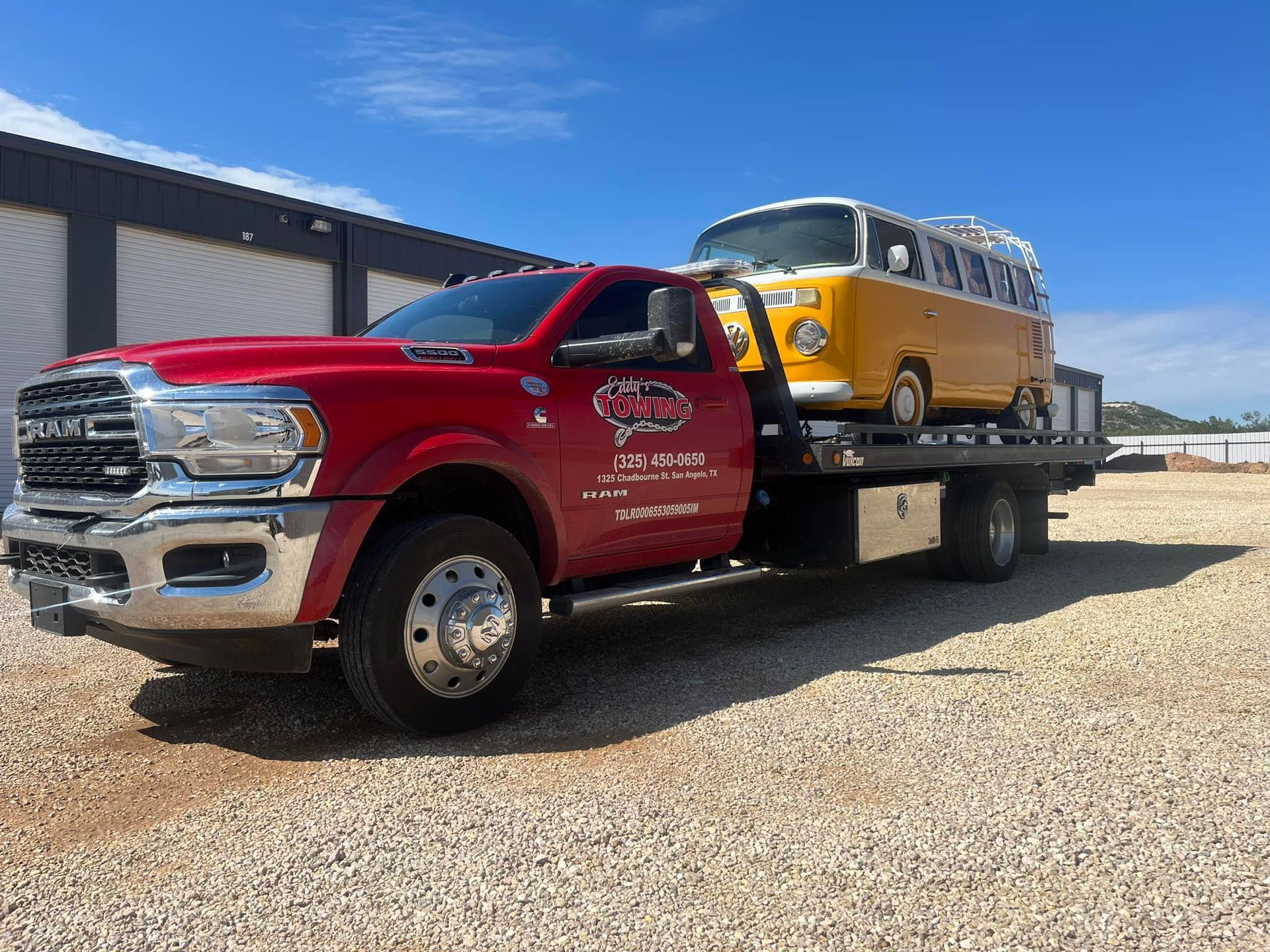 Red tow truck transporting a yellow and white vintage Volkswagen bus on a sunny day.