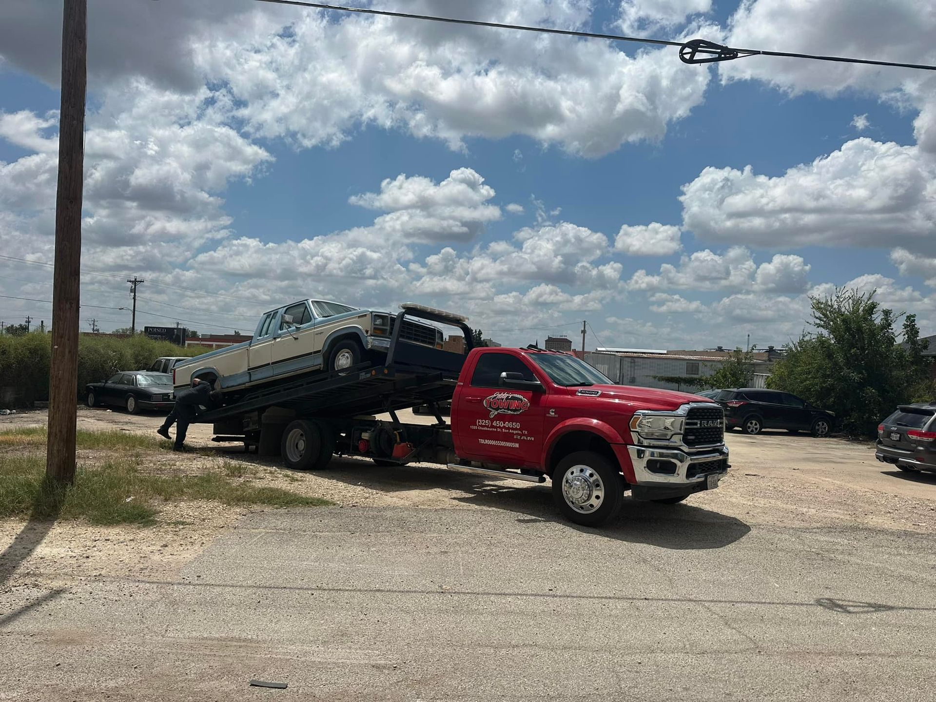 Red tow truck transporting a white car on a sunny day.