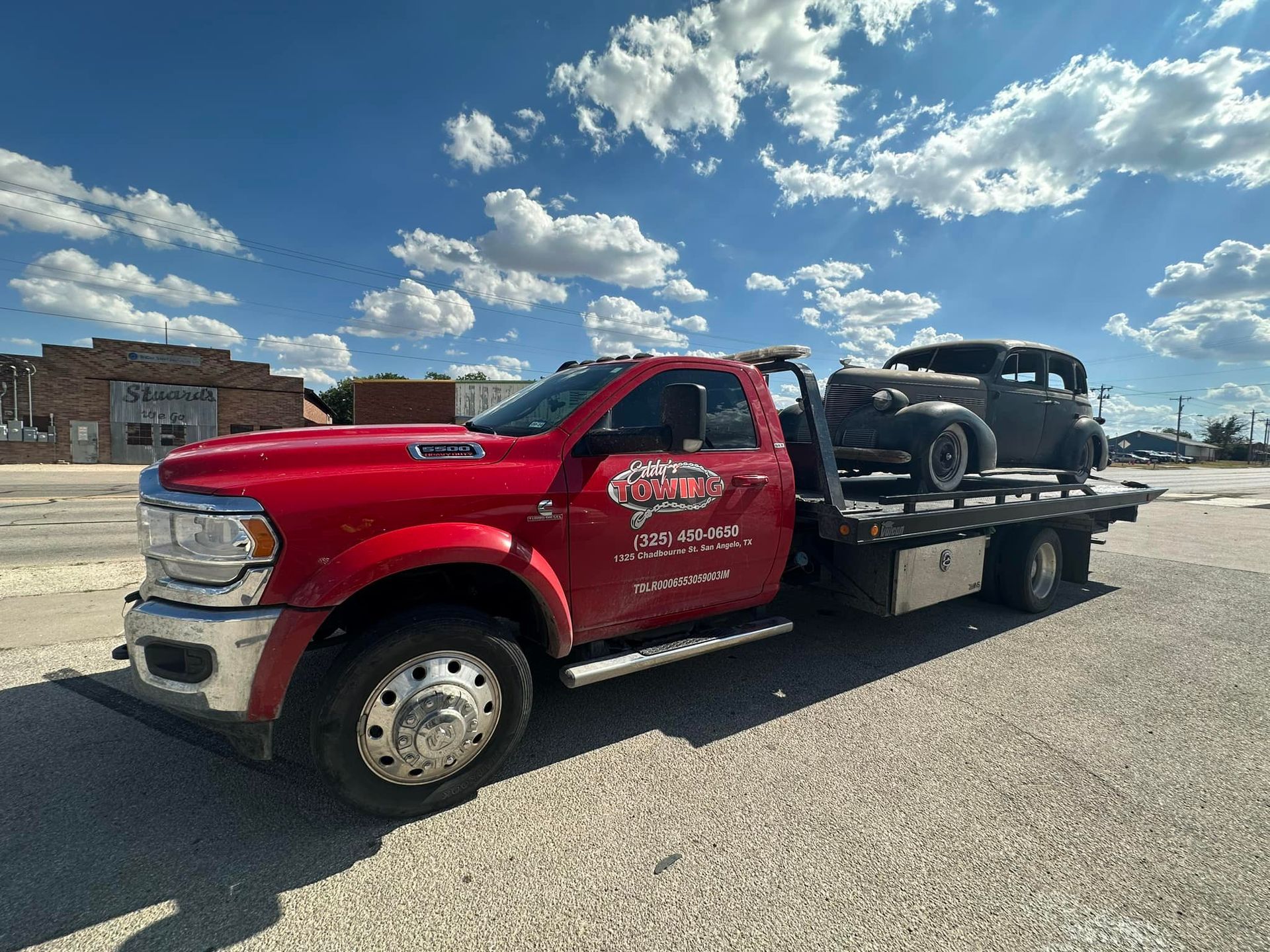 Red tow truck carrying a vintage black car on a sunny day.