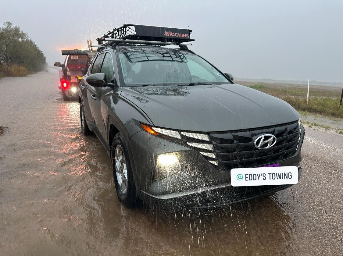 Gray Hyundai Tucson being towed on a flooded road, with a roof rack and camper.