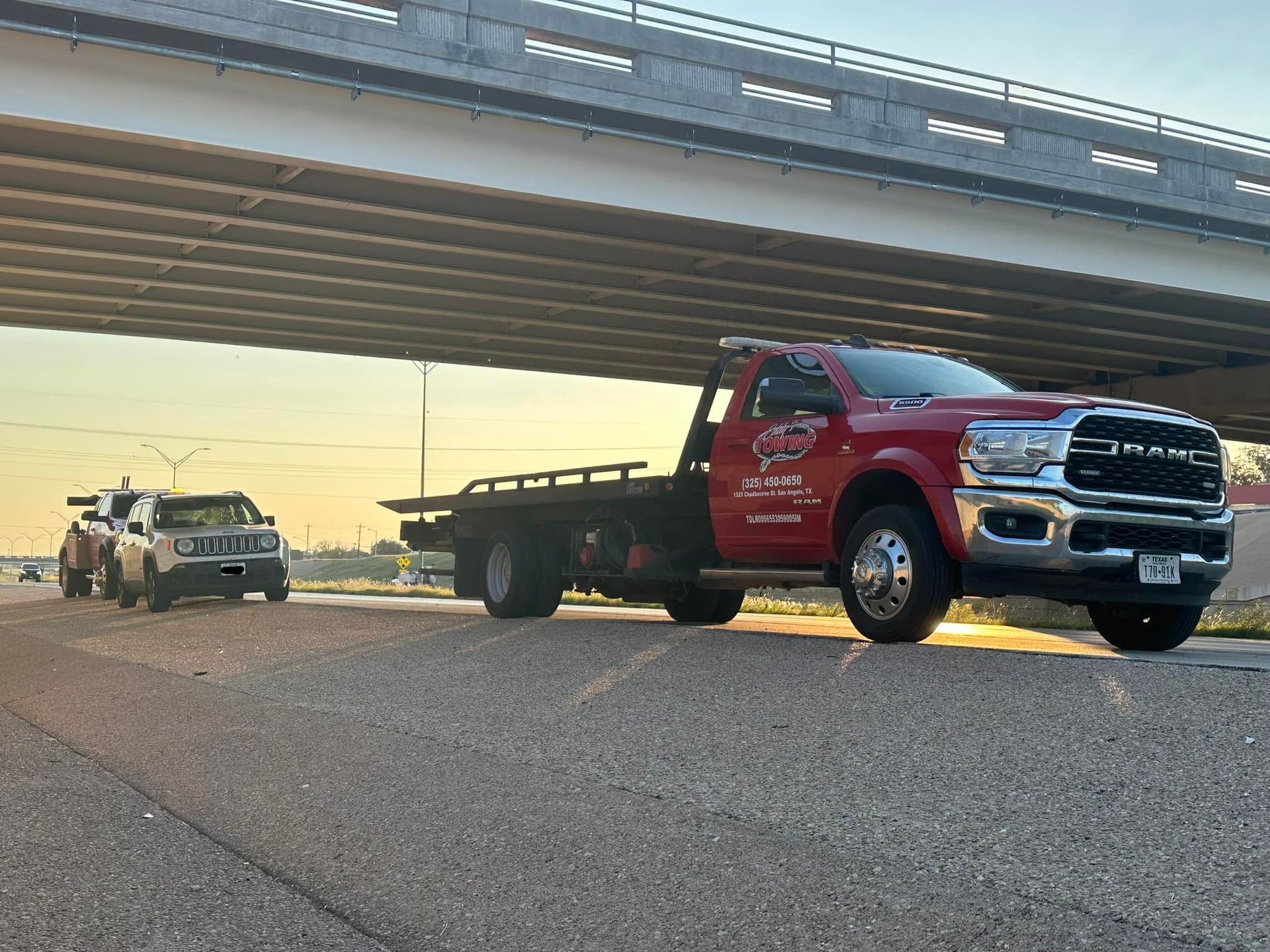 A red tow truck towing a car on a road under a bridge.