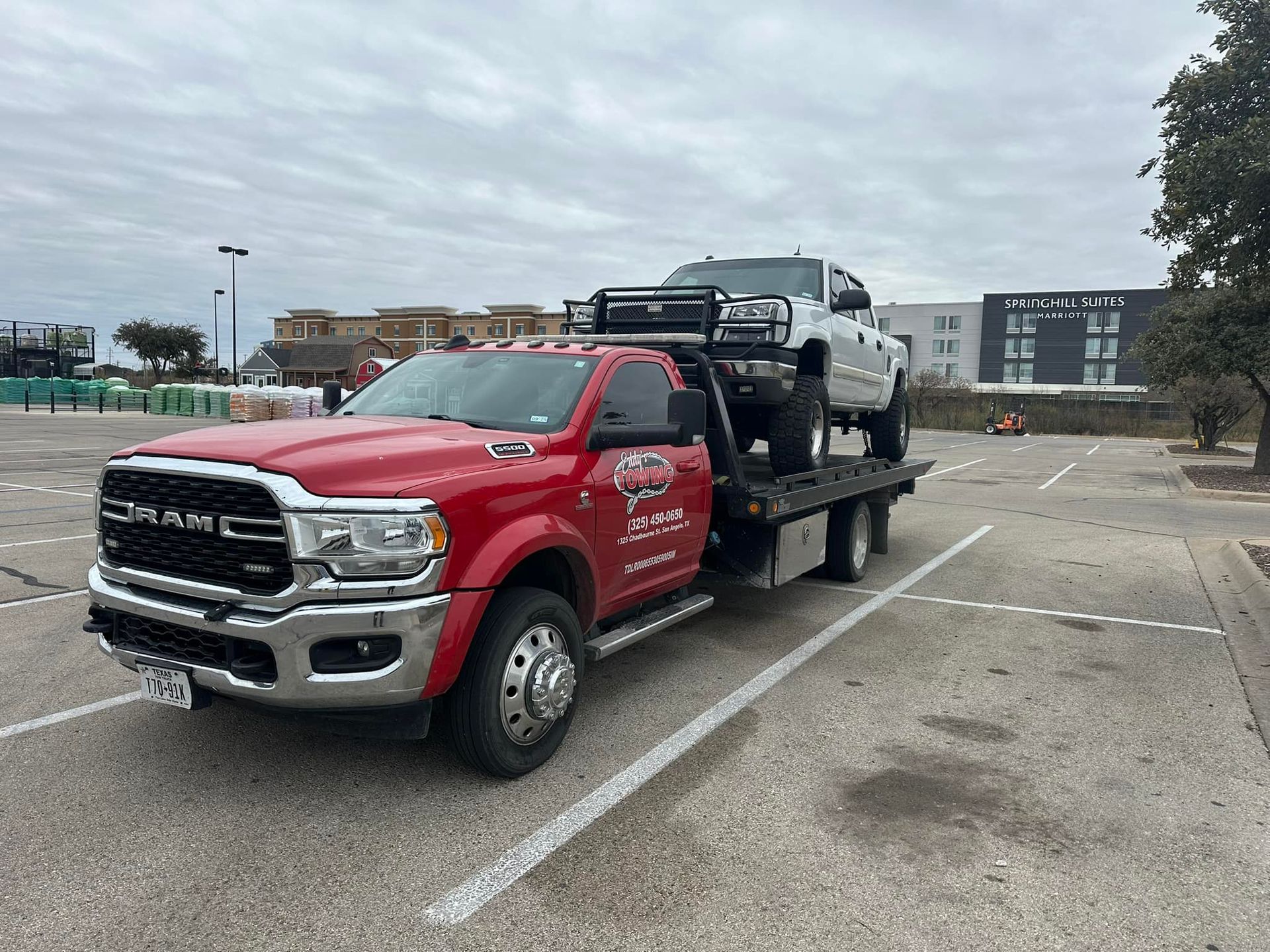 Red tow truck with a white truck loaded on its flatbed, parked in a parking lot.