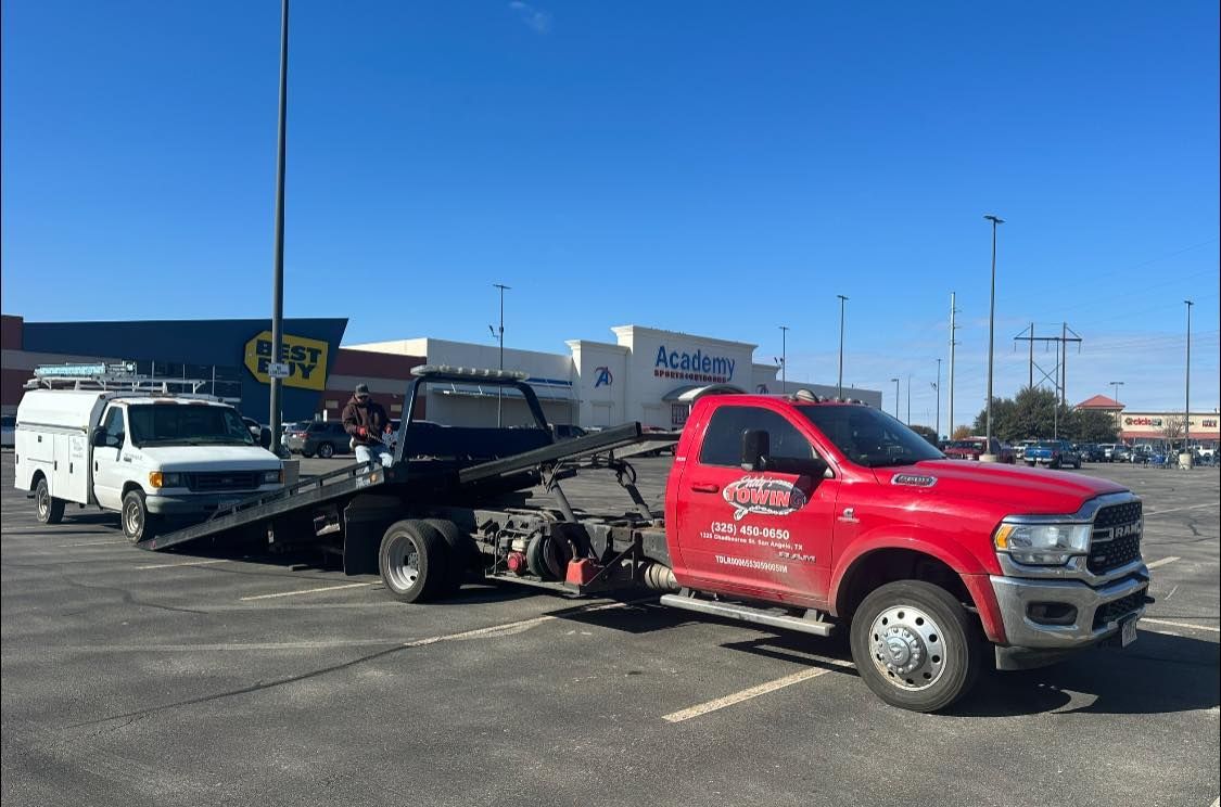 Red tow truck towing a white work van in a parking lot on a sunny day.