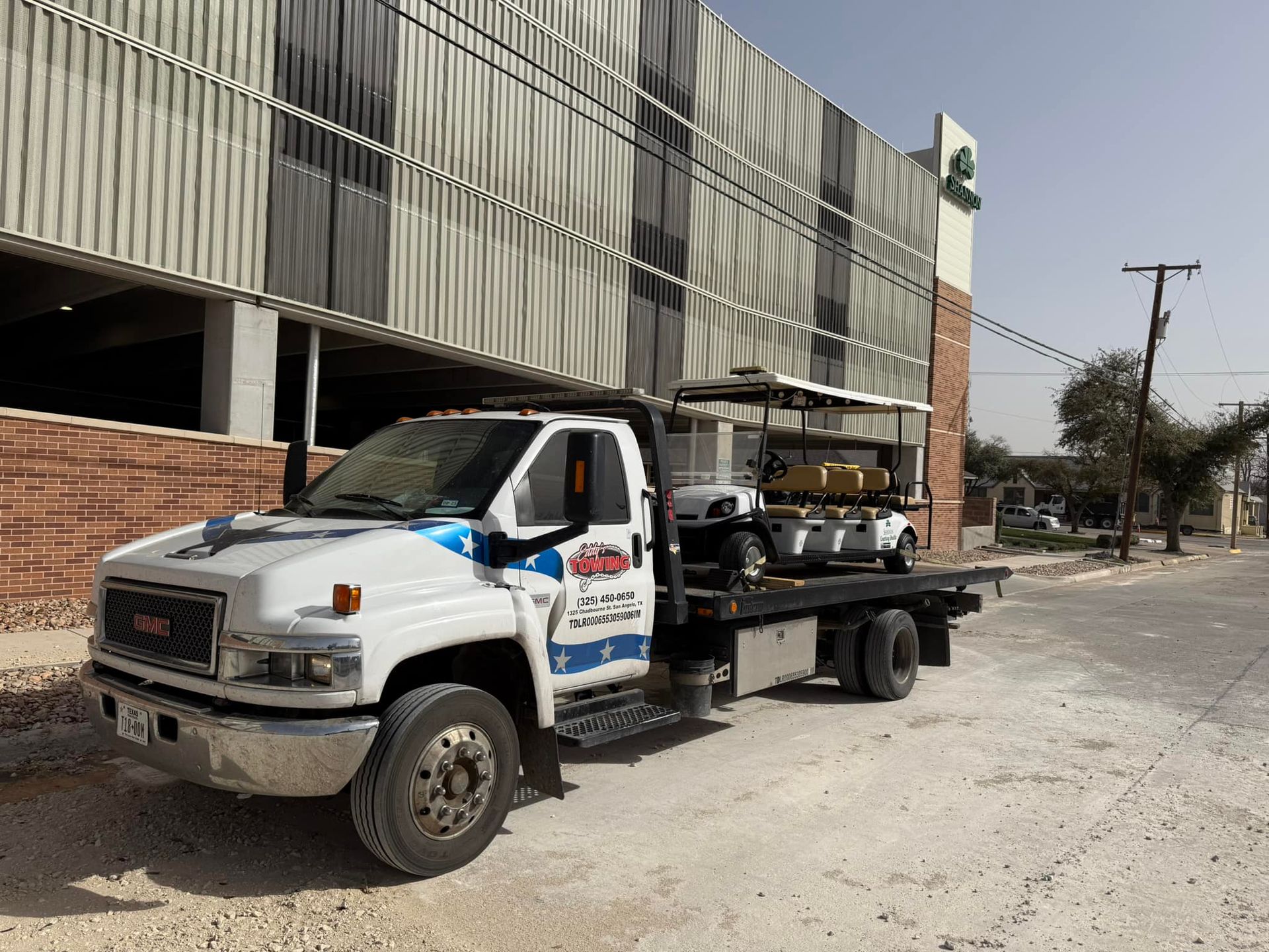 Tow truck parked on a dirt road, in front of a building under construction.
