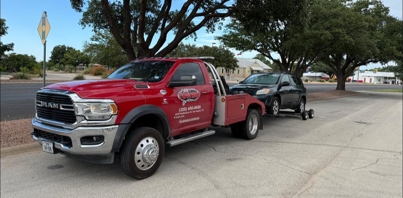 Red tow truck towing a black SUV on a paved area, trees in the background.
