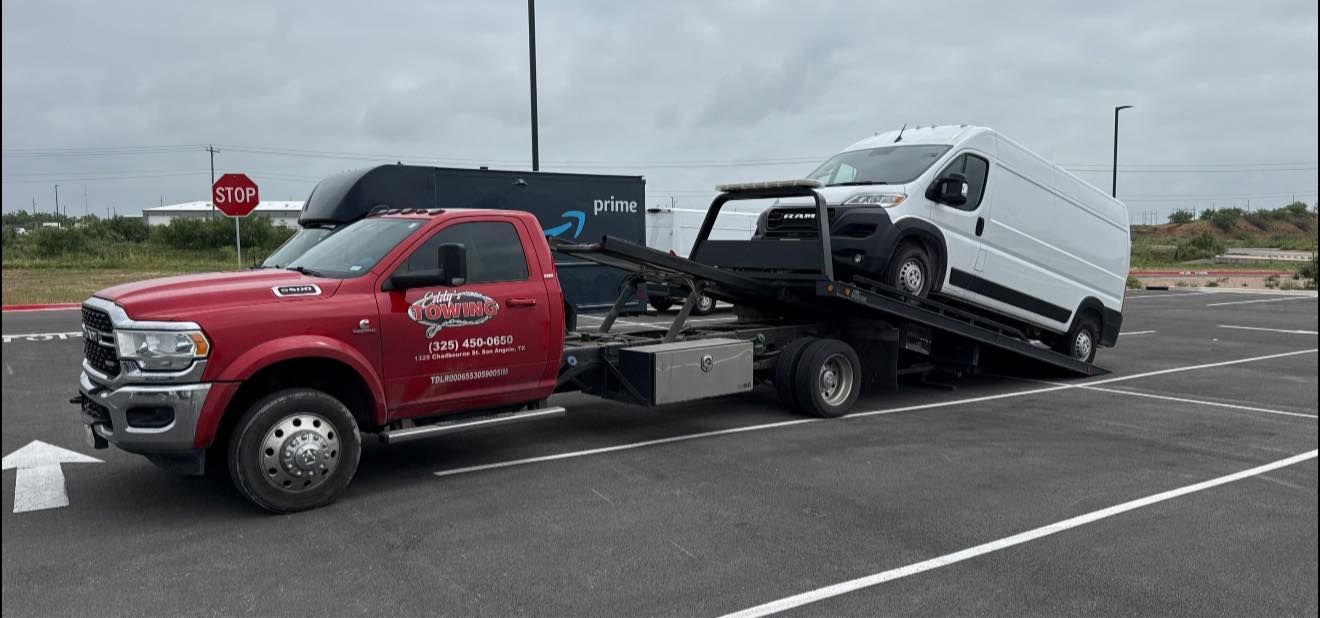 A red tow truck carrying a white van on a flatbed in a parking lot.