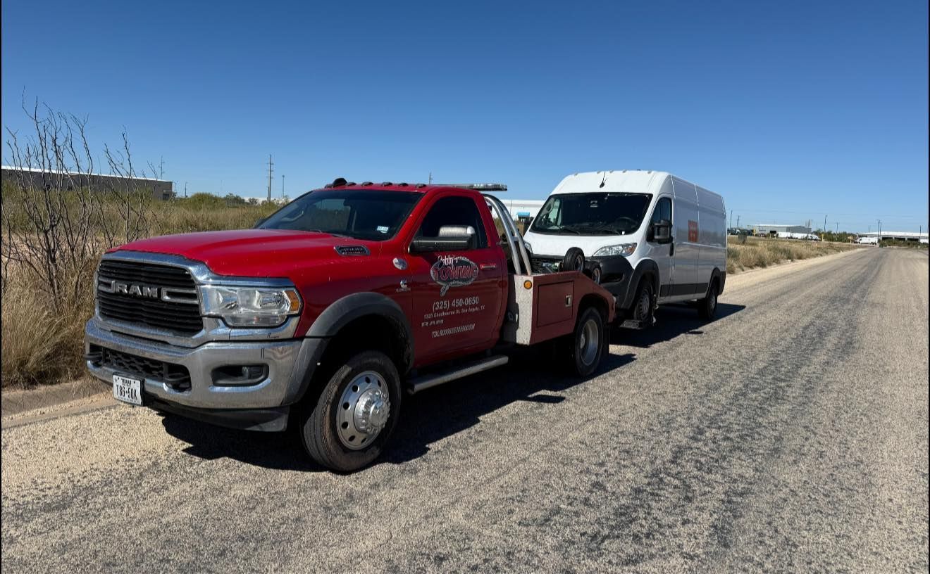 Red tow truck towing a white van on a dirt road under a blue sky.
