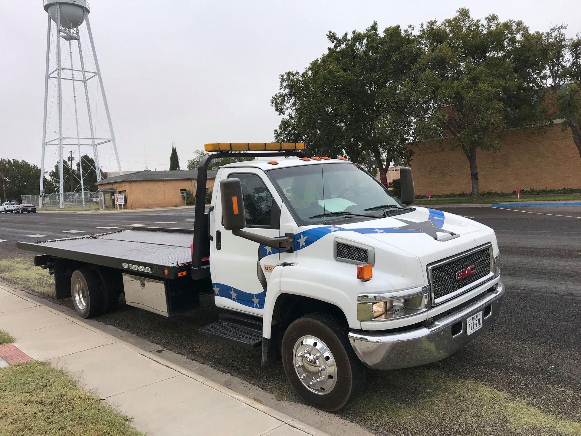White tow truck parked on a street; a water tower is in the background.