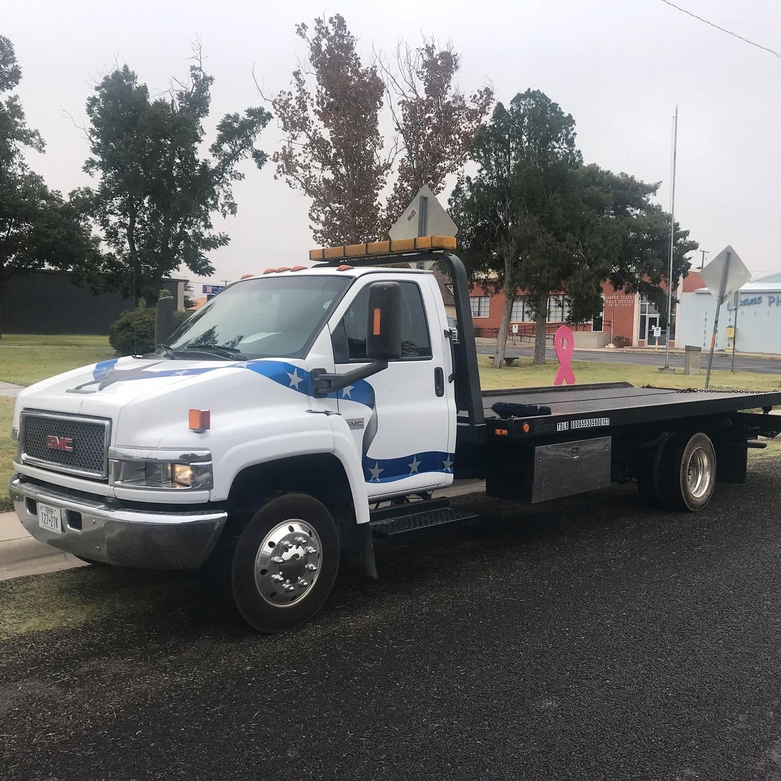 White GMC tow truck on a street, with an empty flatbed.
