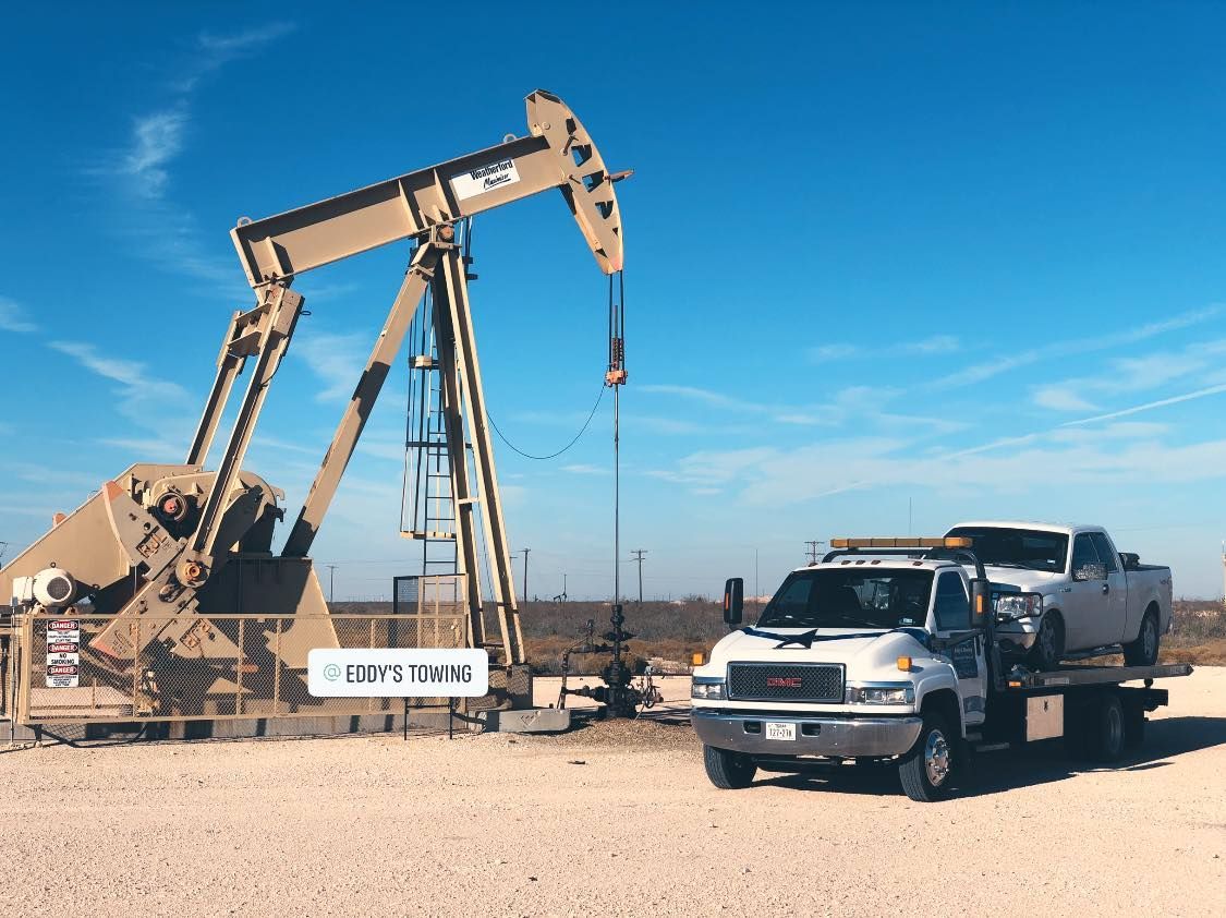 Oil pump jack and tow truck with vehicle under a clear blue sky.