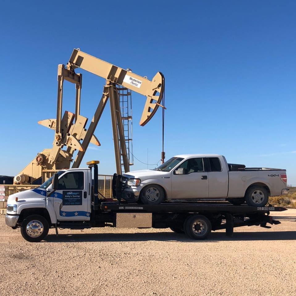 Tow truck with a white pickup, oil pump in background.
