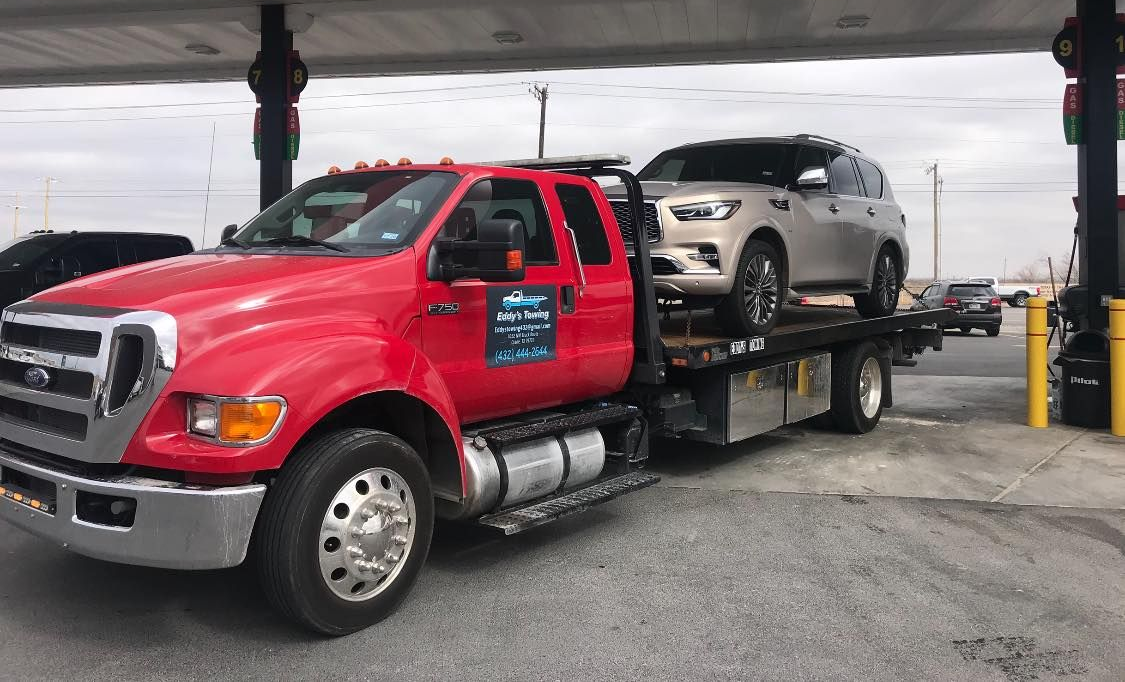 Red tow truck carrying a light-colored SUV at a gas station.