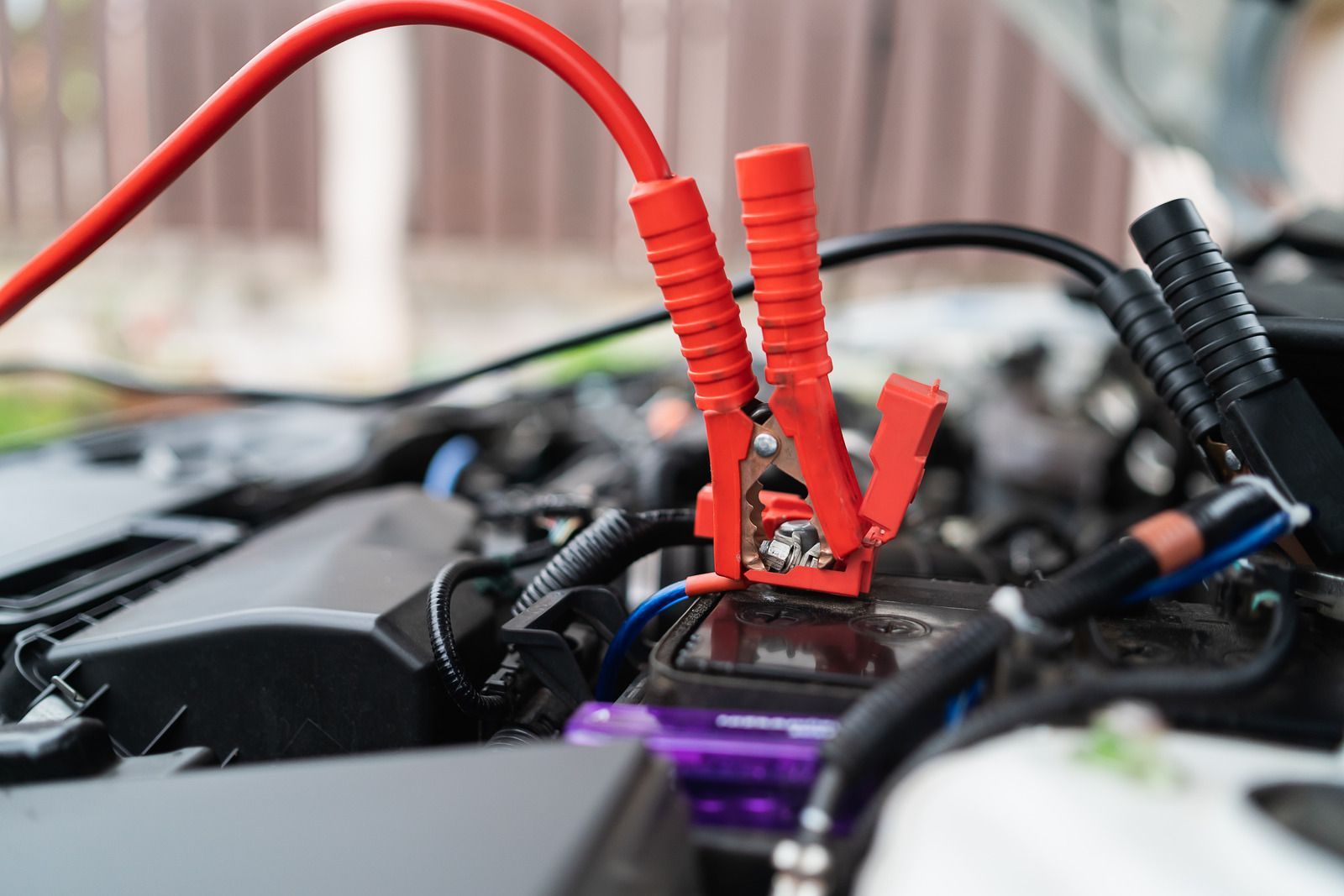 Red jumper cables attached to a car battery under the hood.