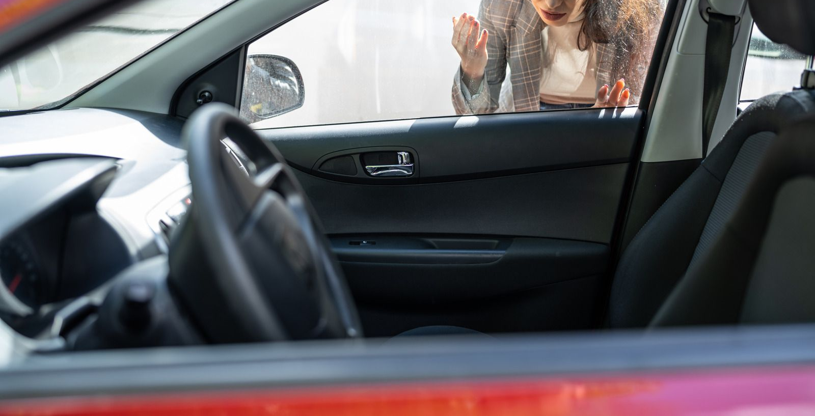 Woman locked out of her car, gesturing frustratedly. Red car interior visible.