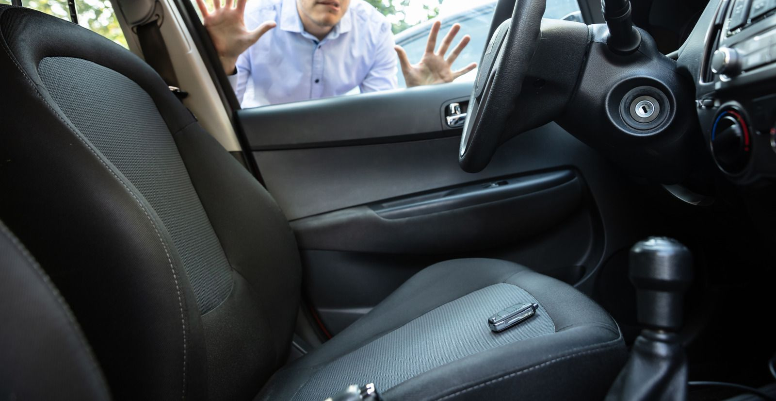 Man locked out of car, key on front seat, hands up against window.