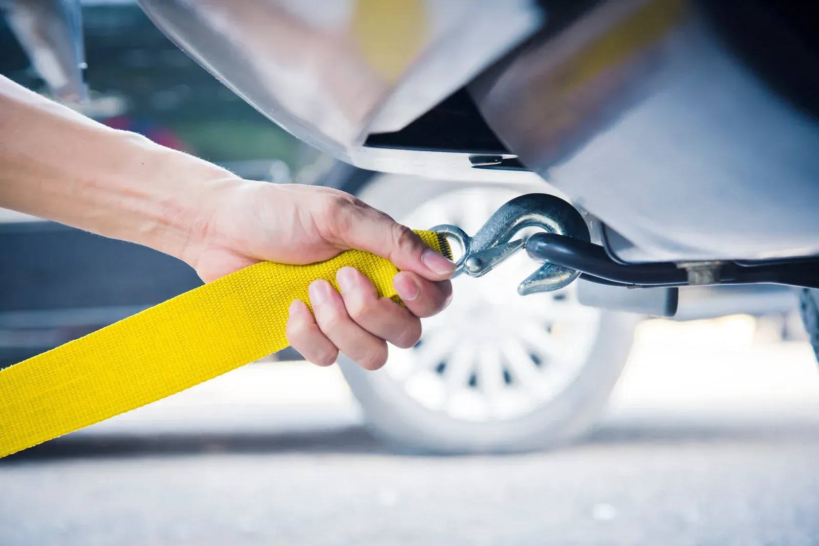 Hand attaching yellow tow strap to a silver vehicle's tow hook.