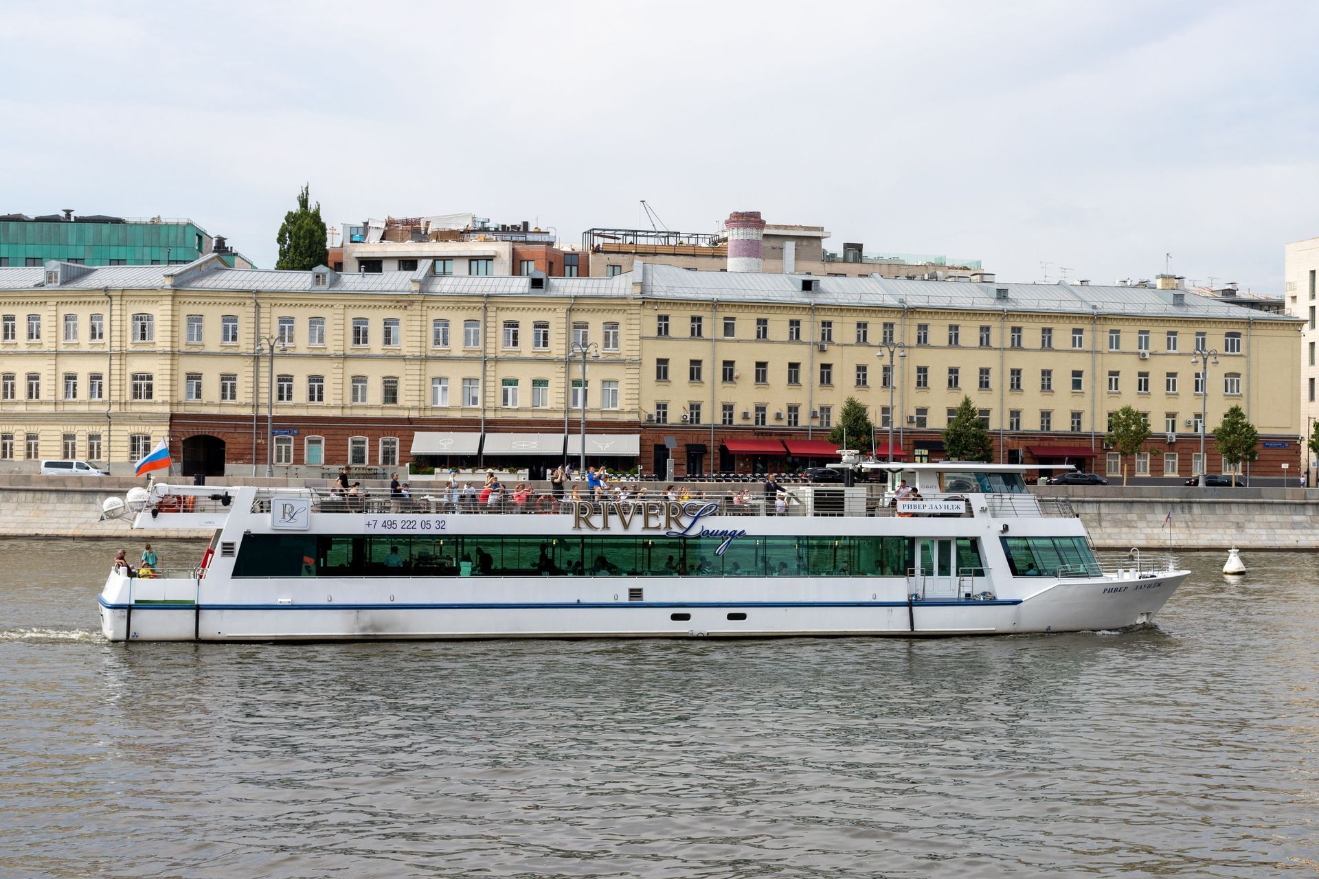White passenger boat on a river with beige waterfront buildings in the background
